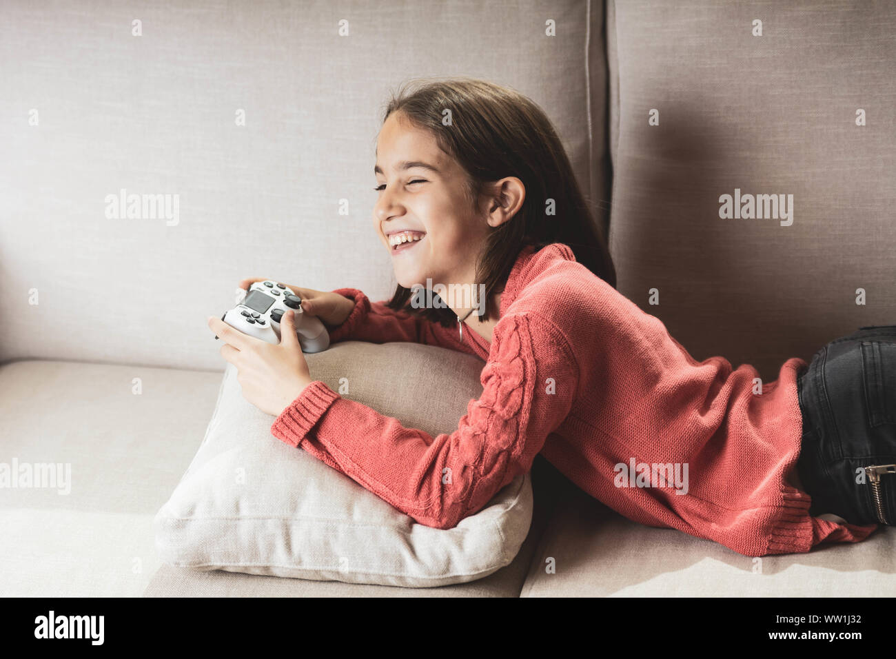 Niña jugando en casa con la videoconsola tumbada en el divani Foto Stock