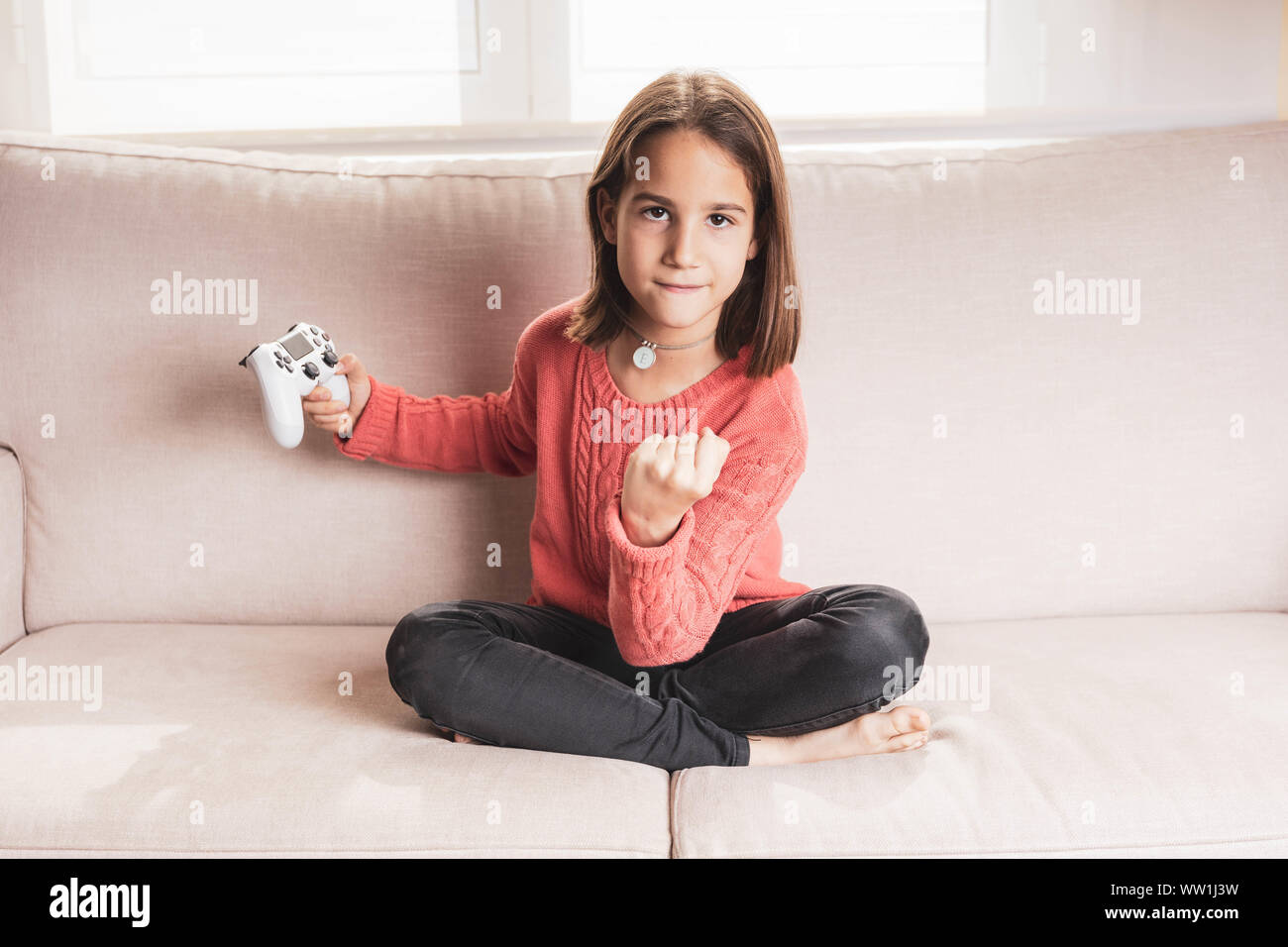 Niña jugando en casa con la videoconsola sentada en el divani Foto Stock