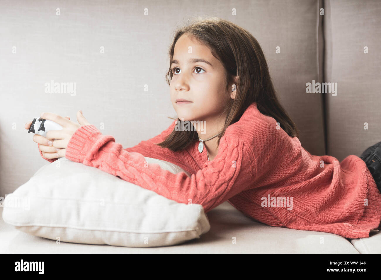 Niña jugando en casa con la videoconsola tumbada en el divani Foto Stock