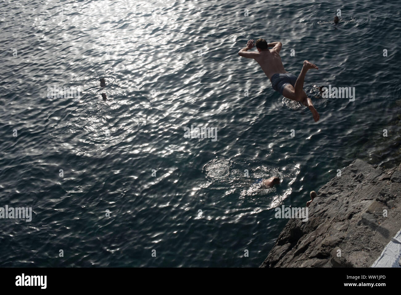 Un subacqueo salta da una scogliera a Manarola, uno dei cinque villaggi di pescatori delle Cinque Terre, nella Riviera Italiana. Foto Stock