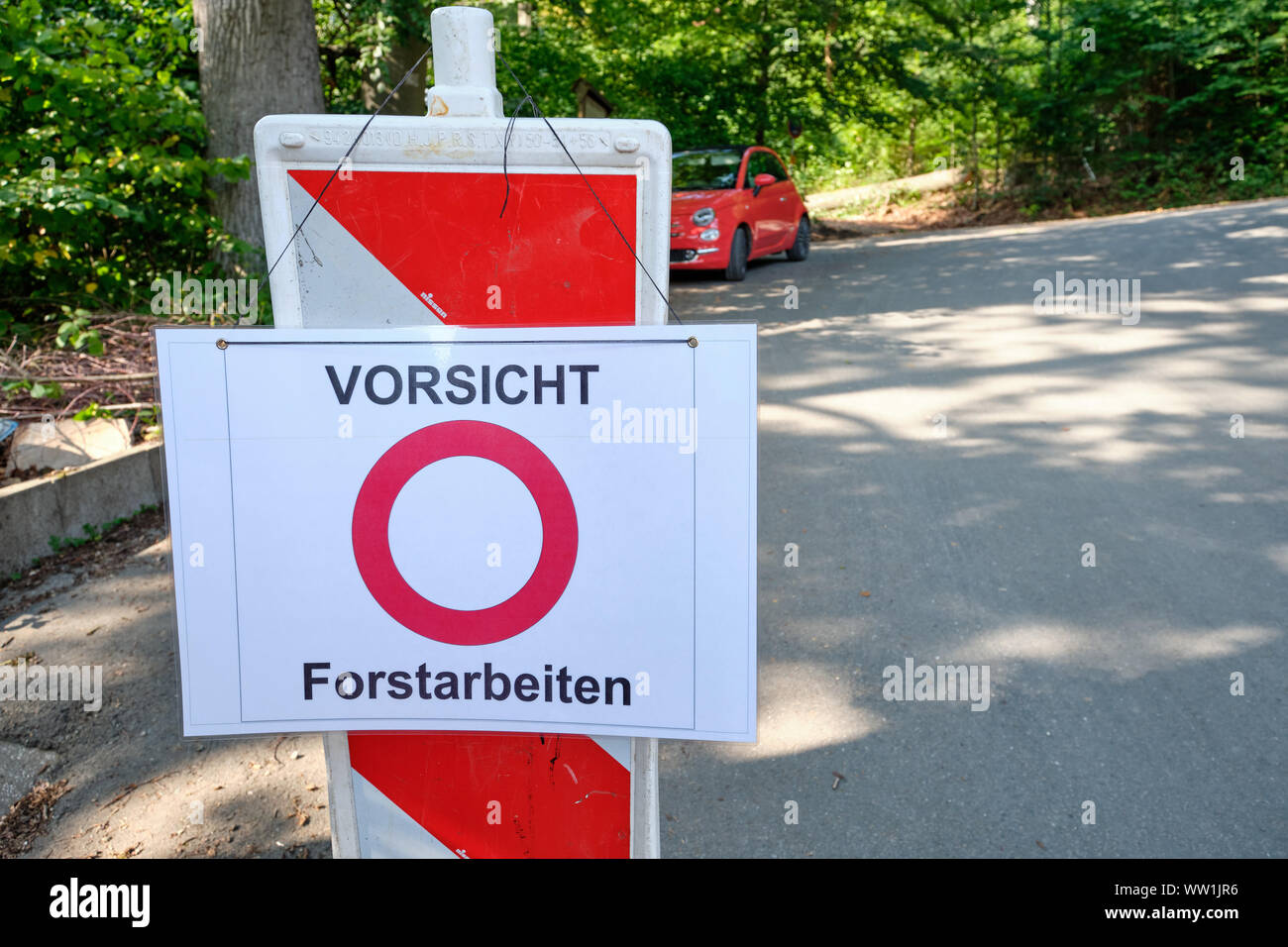 Weissenbach, Germania - 11 Settembre 2019: Un selfmade segno di traffico su una strada di campagna di fronte ad un auto rossa e foresta dice 'Vorsicht Forstarbeiten Foto Stock