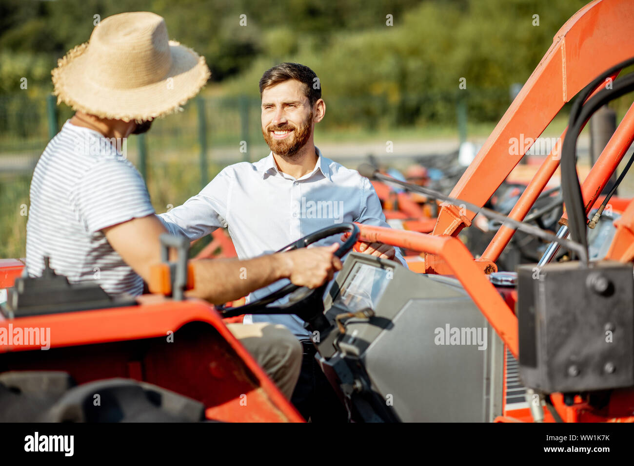 Giovani agronomo con eleganti venditore scegliendo un trattore per l'agricoltura sul terreno aperto del negozio agricolo Foto Stock