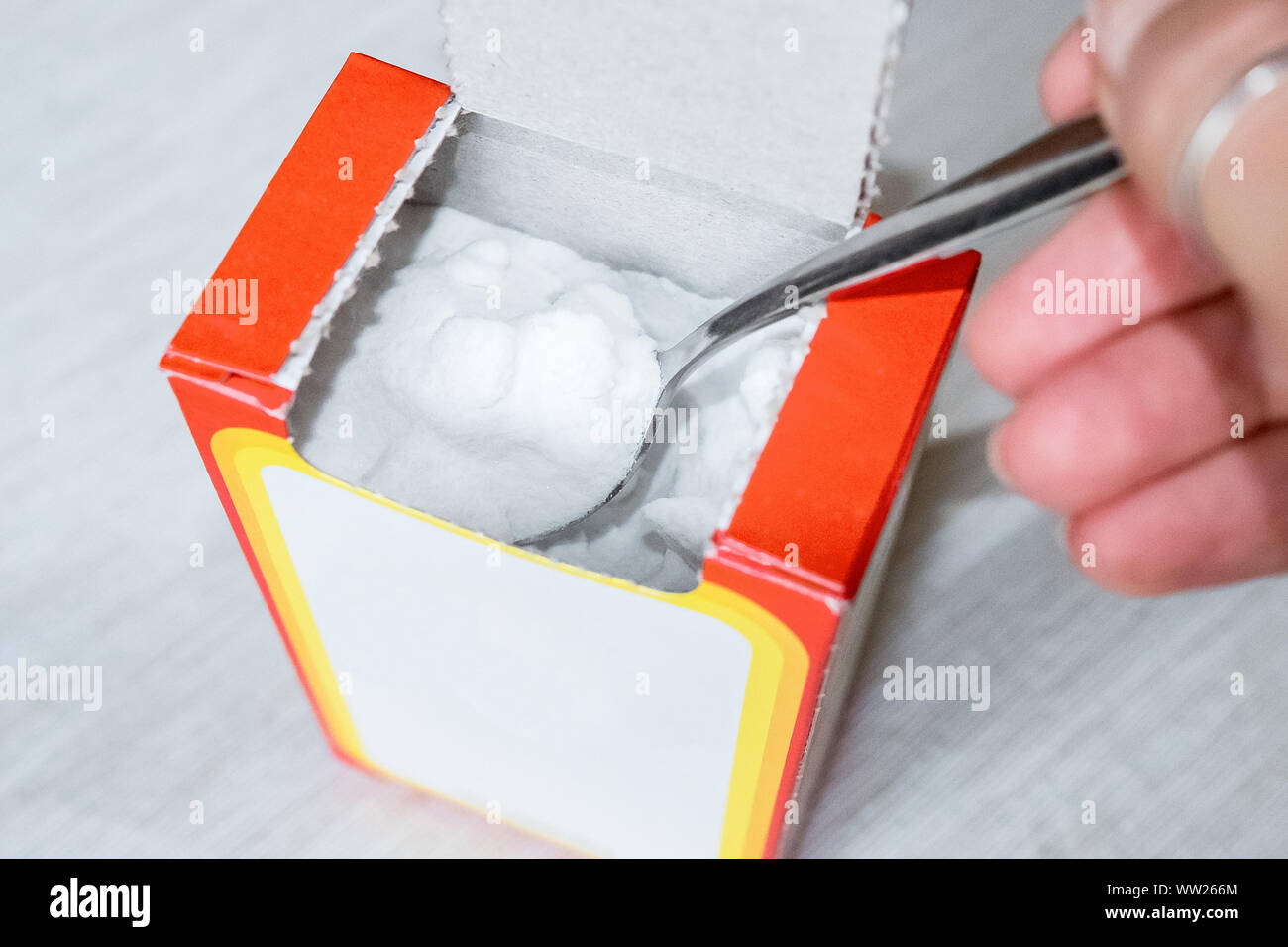 Carbonato di sodio in polvere in un cucchiaio. Soda da una scatola di cartone. La guarnizione sul tavolo in cucina Foto Stock