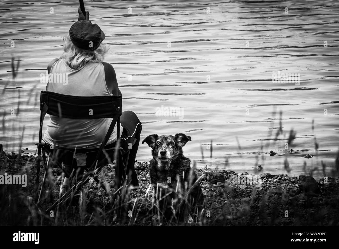 Solo una donna e il suo cane custode sono la pesca sul lago Cassière Foto Stock