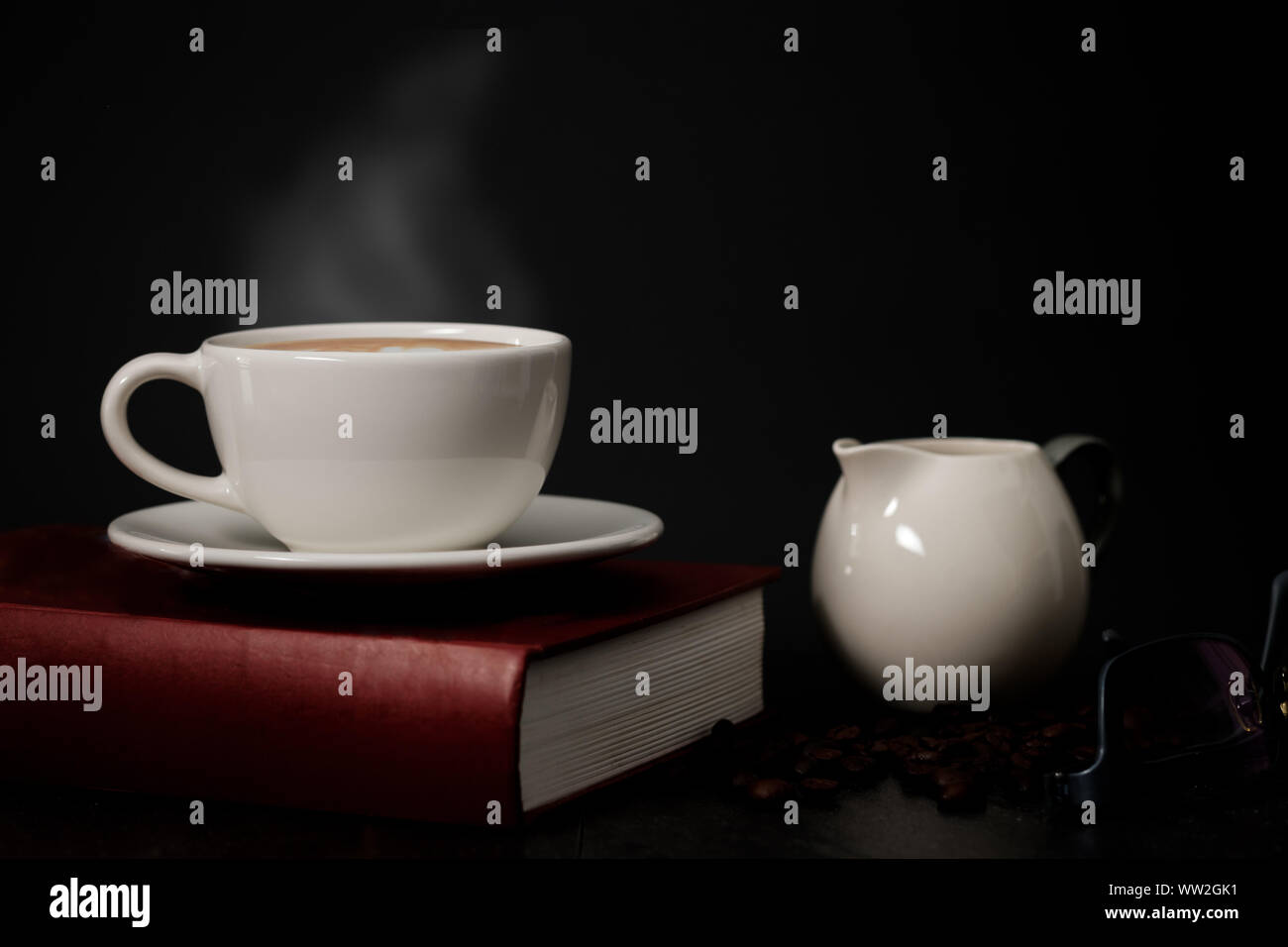 Classic still life - una tazza di caffè con fumo e caffè torrefatto sul vecchio red book, occhiali, hanno uno spazio di copia, luce oscura l'immagine. Foto Stock