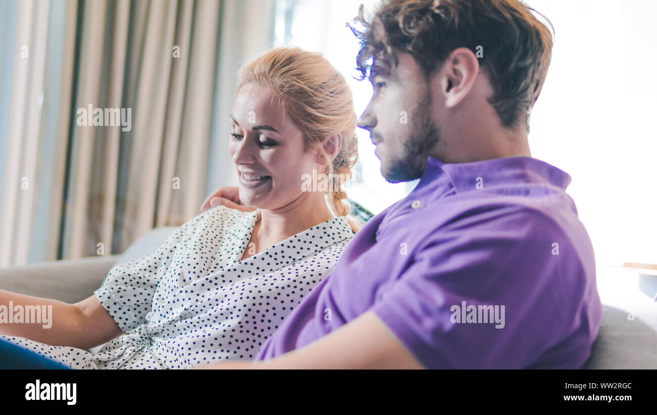 La millenaria matura in amore rilassante insieme sul divano di casa. Coppia felice cercando di ogni altro e ridere. Focus sulla ragazza Foto Stock