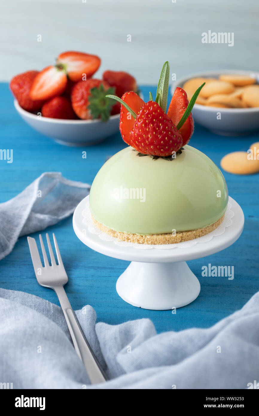 Blue tavolo in legno con no-bake fragola mini sfera matcha cheesecake con coppa di sale caramello, buiscuits e fragole fresche, vetro di piazzole e Foto Stock