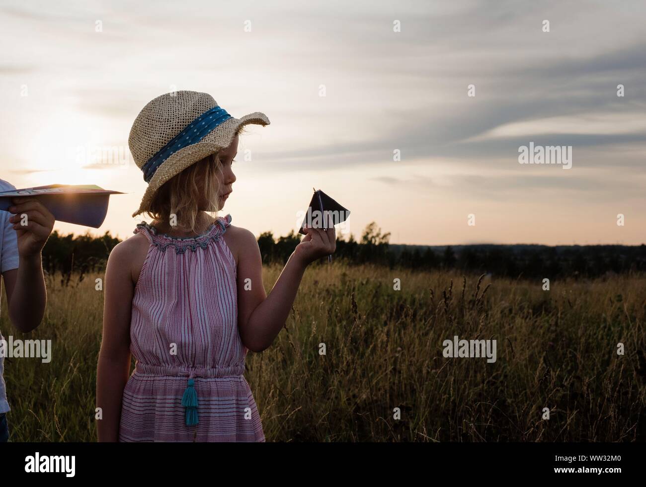 Profilo di una giovane ragazza con un aeroplano di carta in un prato al tramonto Foto Stock