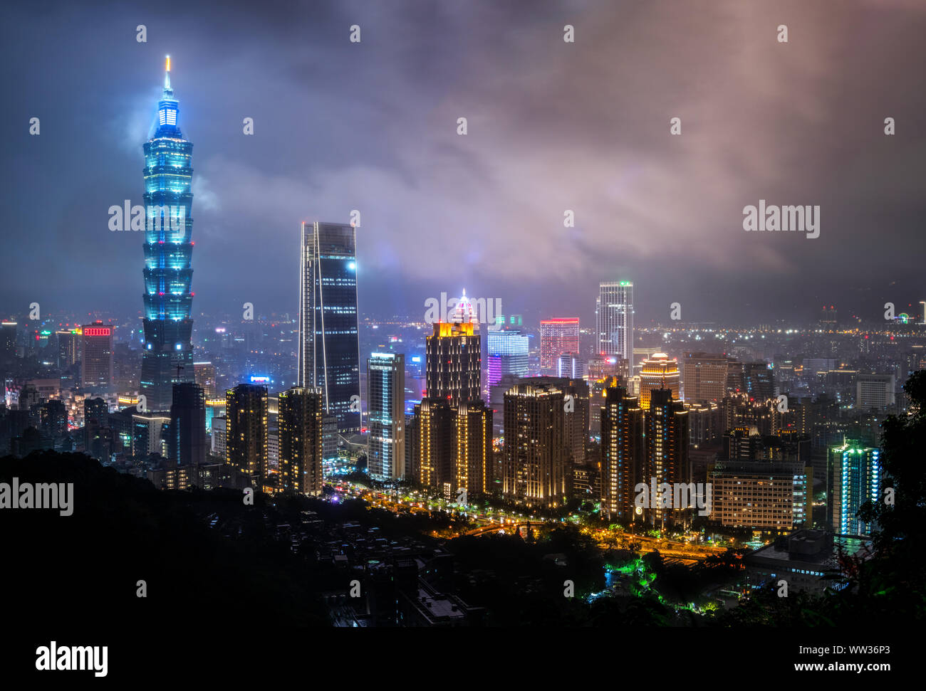 Taiwan: Misty nuvole passare la sommità del grattacielo Taipei 101 di notte illuminata da luci blu. Lo Skyline di Taipei Foto Stock