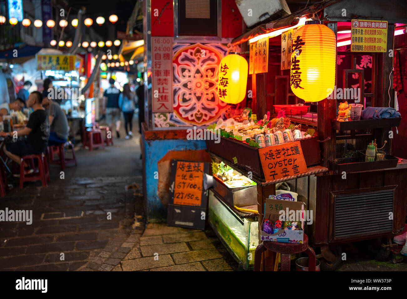 Taipei, Taiwan: piccola cucina di strada in stallo al Mercato Notturno di Raohe decorate con orange lanterne giapponesi, vendita di frutti di mare e birra di Taiwan Foto Stock