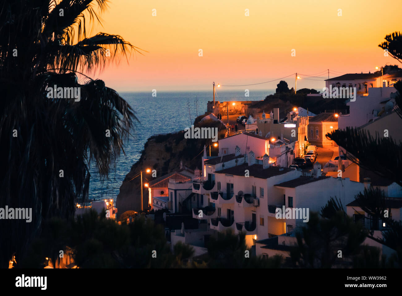 Bella vista di una palma, case mediterranee e un tramonto a Carvoeiro Beach in Algarve, PORTOGALLO Foto Stock