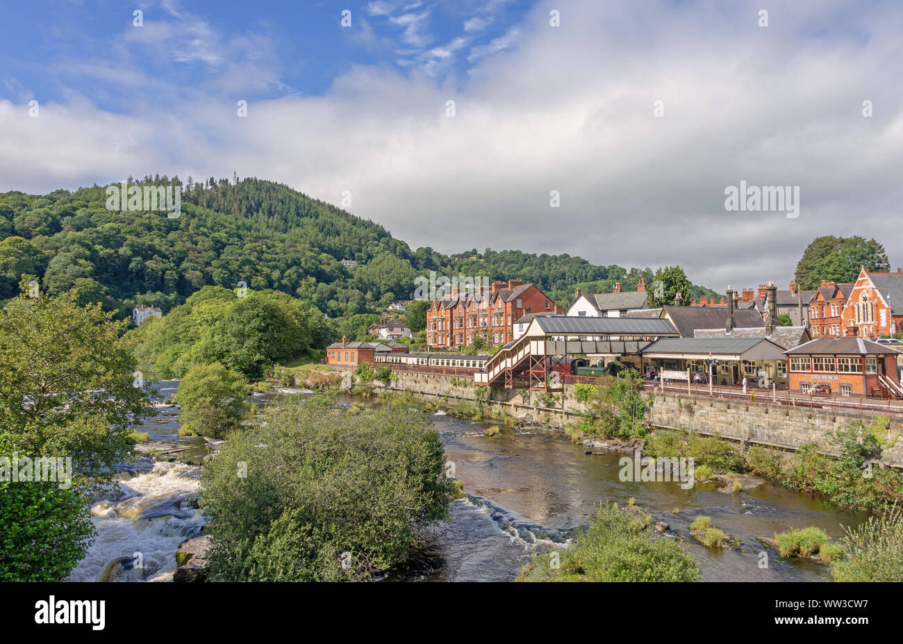 Llangollen Railway Station da tutta la veloce-fluente fiume Dee. Un albero coperto hill è in background e il cielo nuvoloso è sopra. Foto Stock