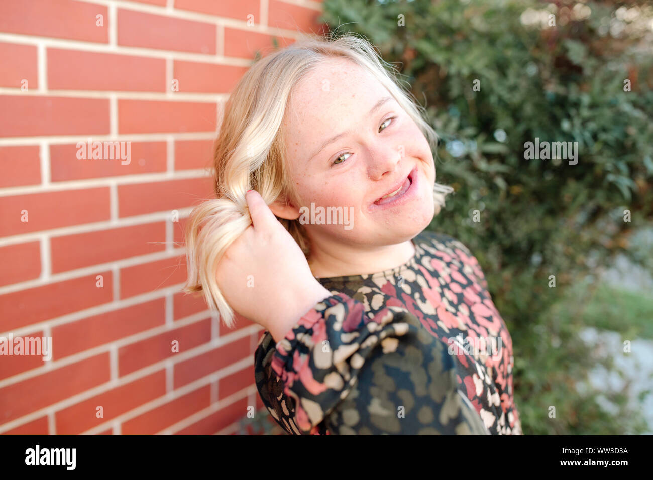 Sorridente ragazza adolescente con sindrome di Down capovolge i capelli al di fuori nella luce del sole Foto Stock