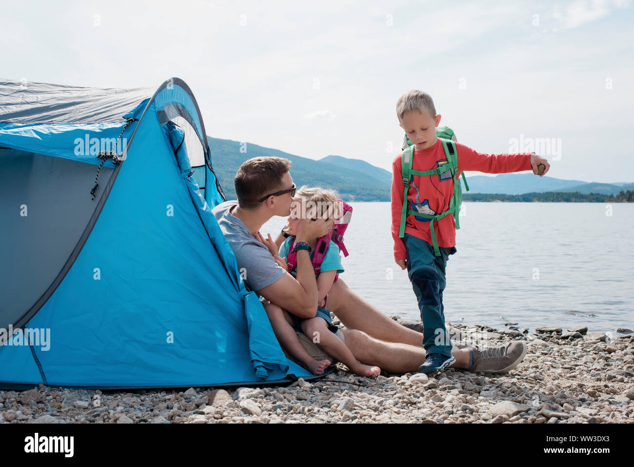 Padre baciare la figlia mentre la sua famiglia gioca il campeggio in riva al mare Foto Stock
