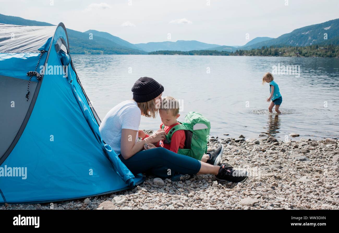 Madre baciare il suo figlio mentre in campeggio in una tenda con la famiglia da mare Foto Stock