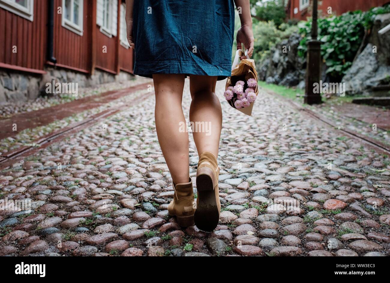 Le femmine le gambe a camminare su una strada acciottolata holding fiori Foto Stock