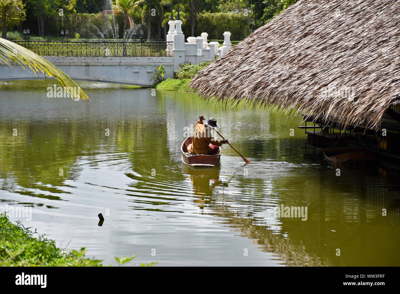 Kanchanaburi, Thailandia, 09.09.2019: un uomo Thailandese in stile tradizionale Tailandese, Siamesi abito canottaggio è un vecchio Thai barca sul lago accanto a una casa galleggiante in t Foto Stock