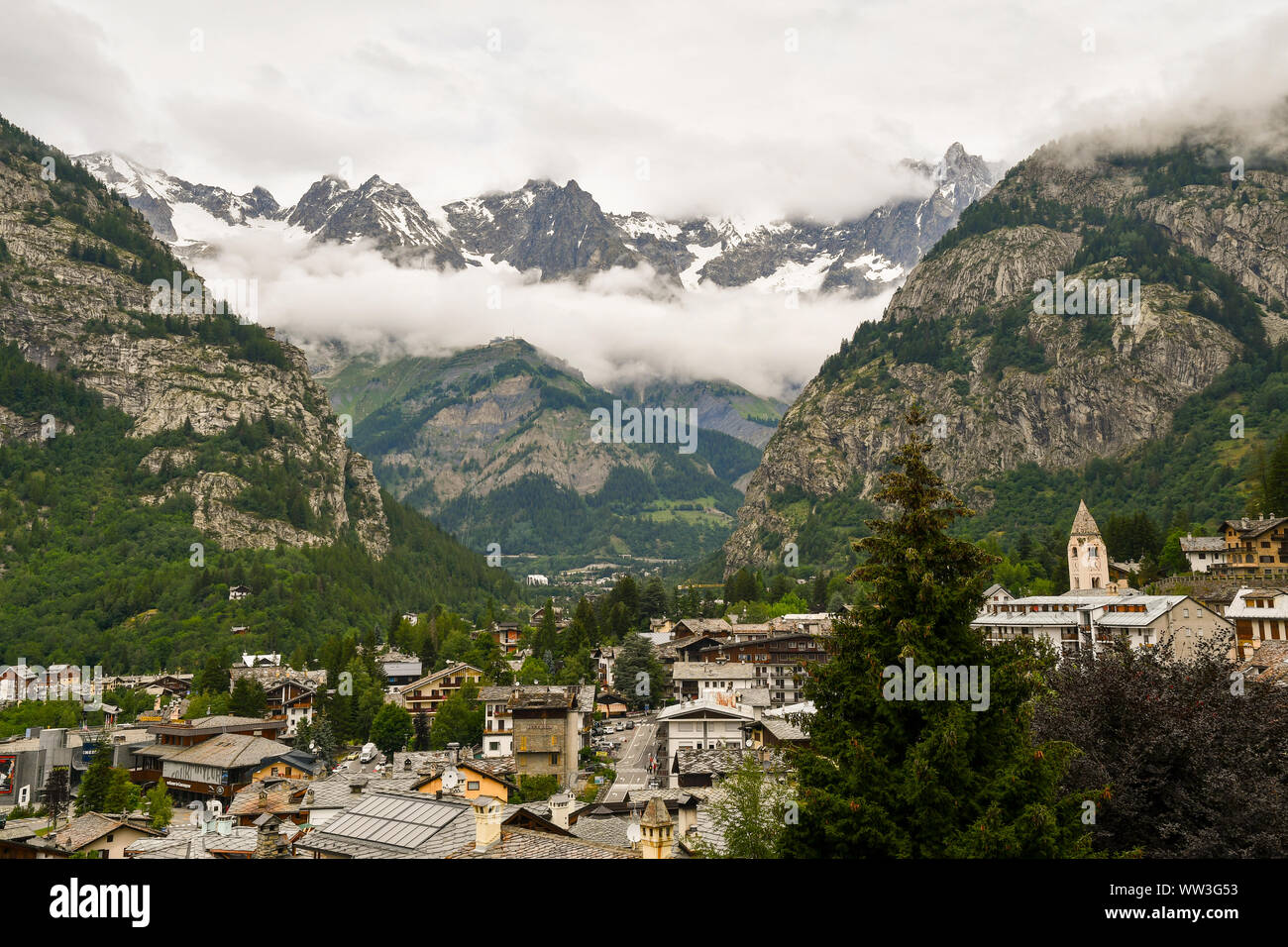 Vista in elevazione di Courmayeur città ai piedi della catena montuosa del Monte Bianco con un cielo nuvoloso in estate, Valle d'Aosta, Alpi, Italia Foto Stock