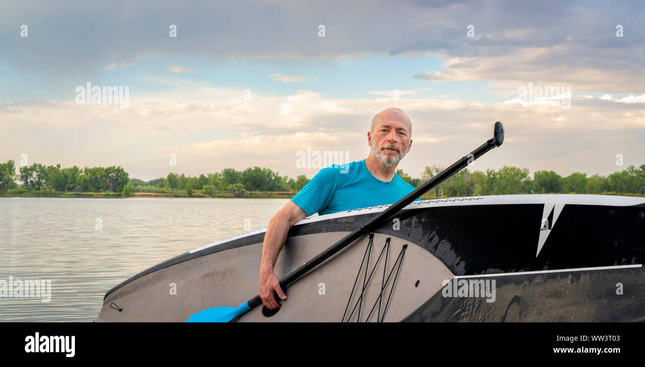 64 anni di vecchio uomo con uno stand up paddleboard dopo paddling allenamento sulle sponde di un lago in Colorado, attivo concetto senior Foto Stock