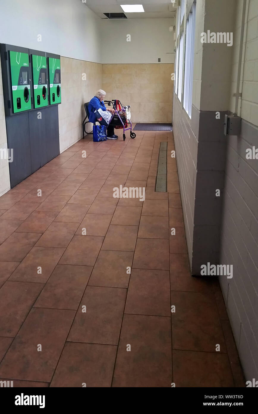 Cromwell, CT, Stati Uniti d'America. Settembre 2019. Una donna anziana seduta da soli all'interno di una camera di riciclaggio con un deambulatore trovare qualcosa mentre si è in attesa per i mezzi di trasporto pubblico Foto Stock