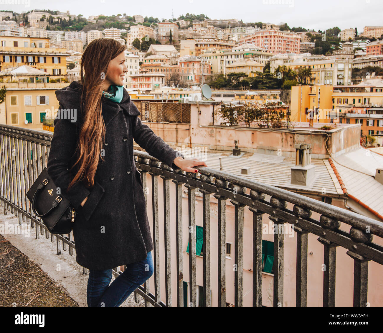 Una ragazza con i capelli lunghi in un mantello guarda il panorama di Genova, carino case e tetti Foto Stock