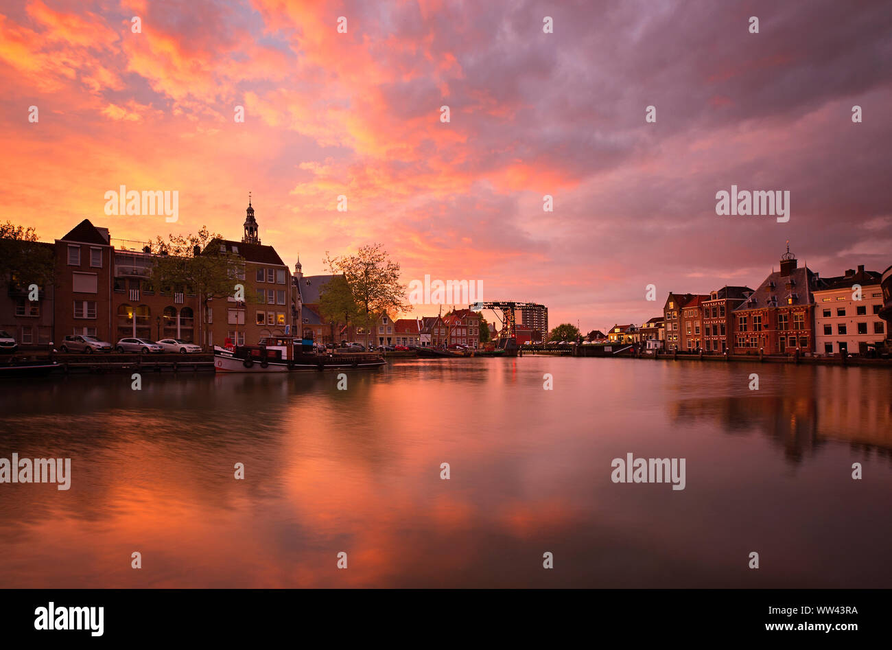 Il centro storico di Maassluis, Paesi Bassi lungo il porto. Sunrise si illumina dietro di antichi edifici vecchi. Tramonto dietro la vecchia chiesa. Paesaggio panoramico Foto Stock