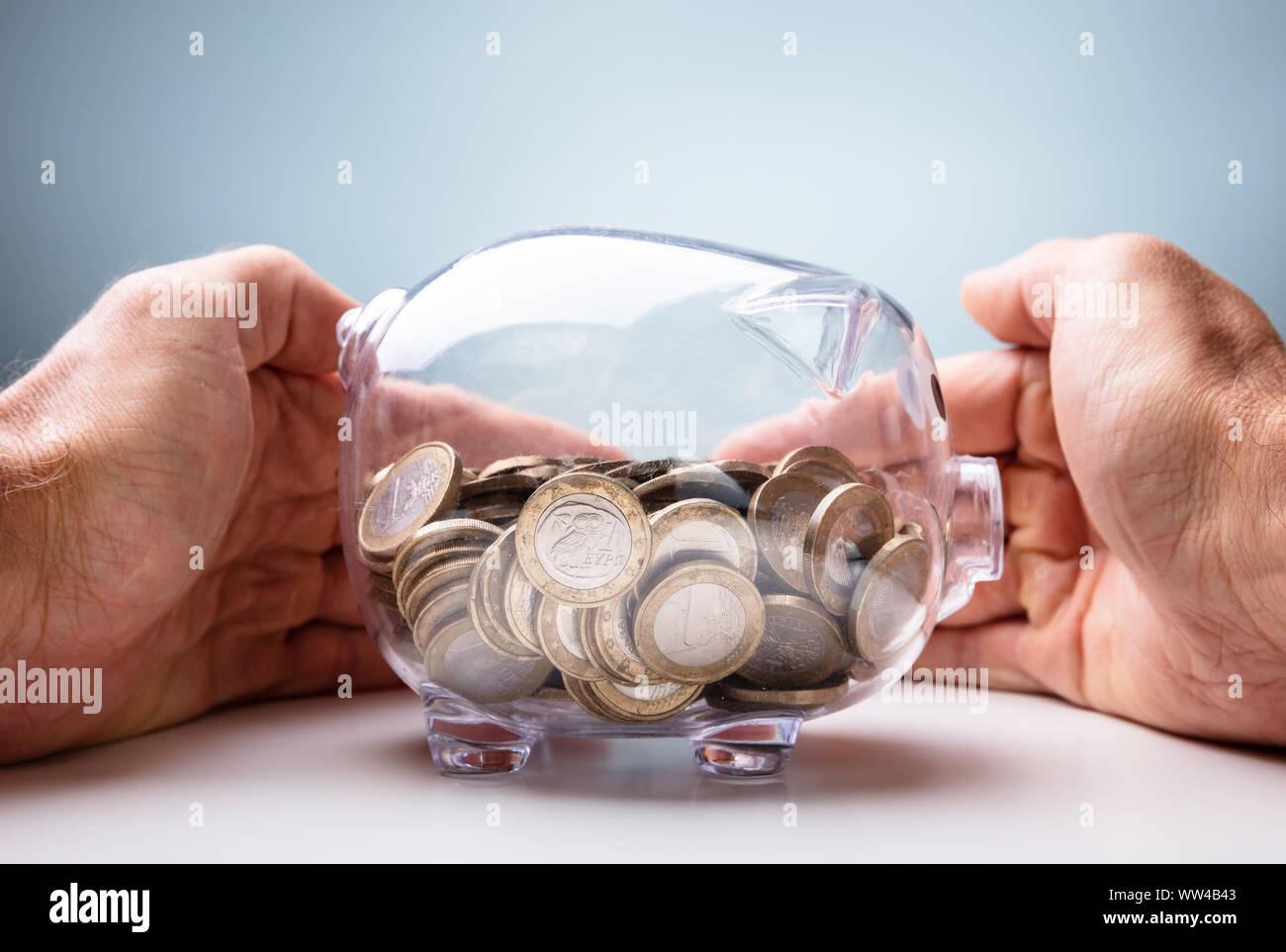 Sezione mediana di imprenditrice la protezione delle monete in euro In trasparente Piggybank al tavolo di legno Foto Stock