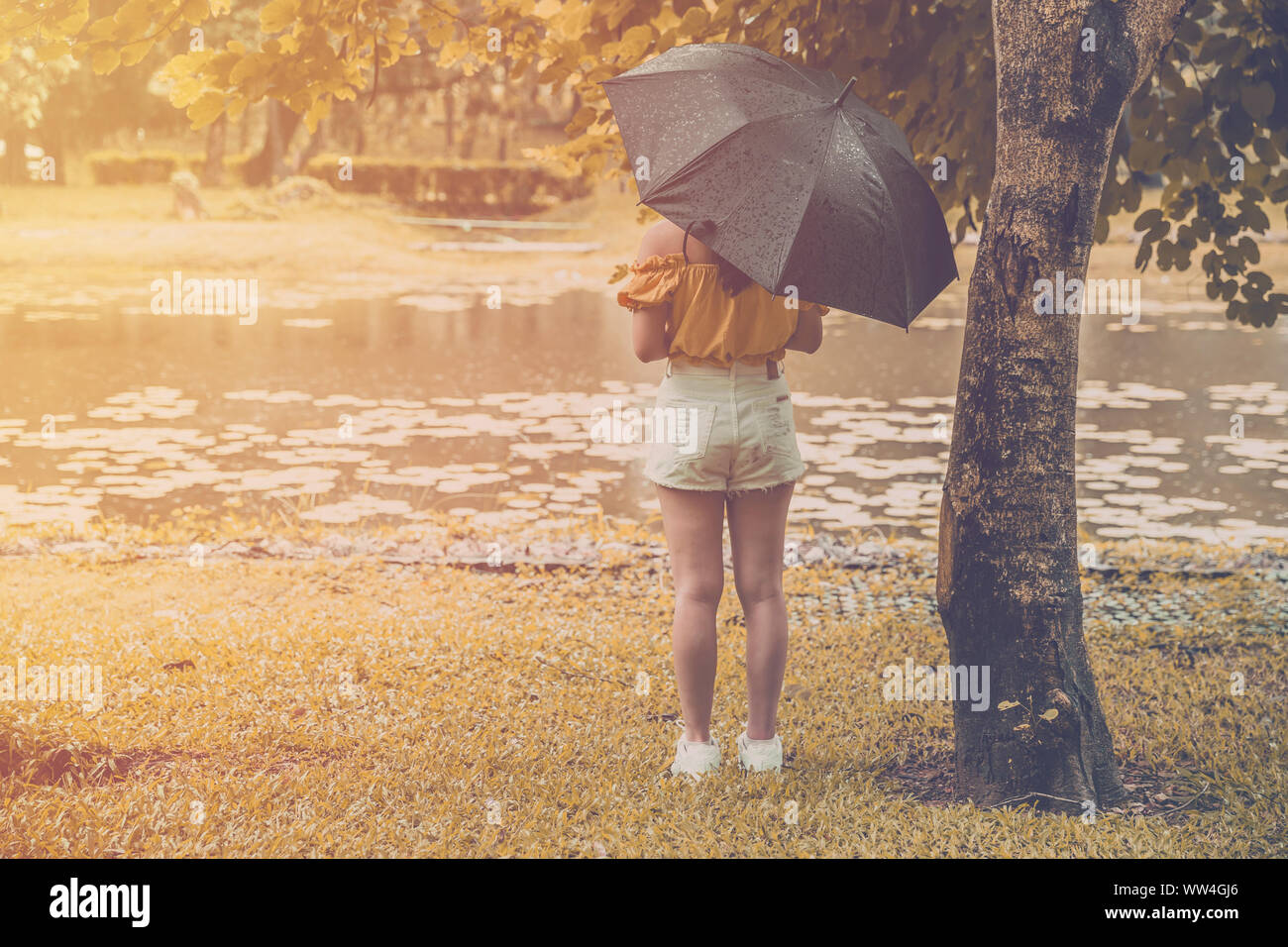 La solitudine adolescente giovane ragazza stand alone in giornata piovosa con tree Park Lake con spazio di copia Foto Stock