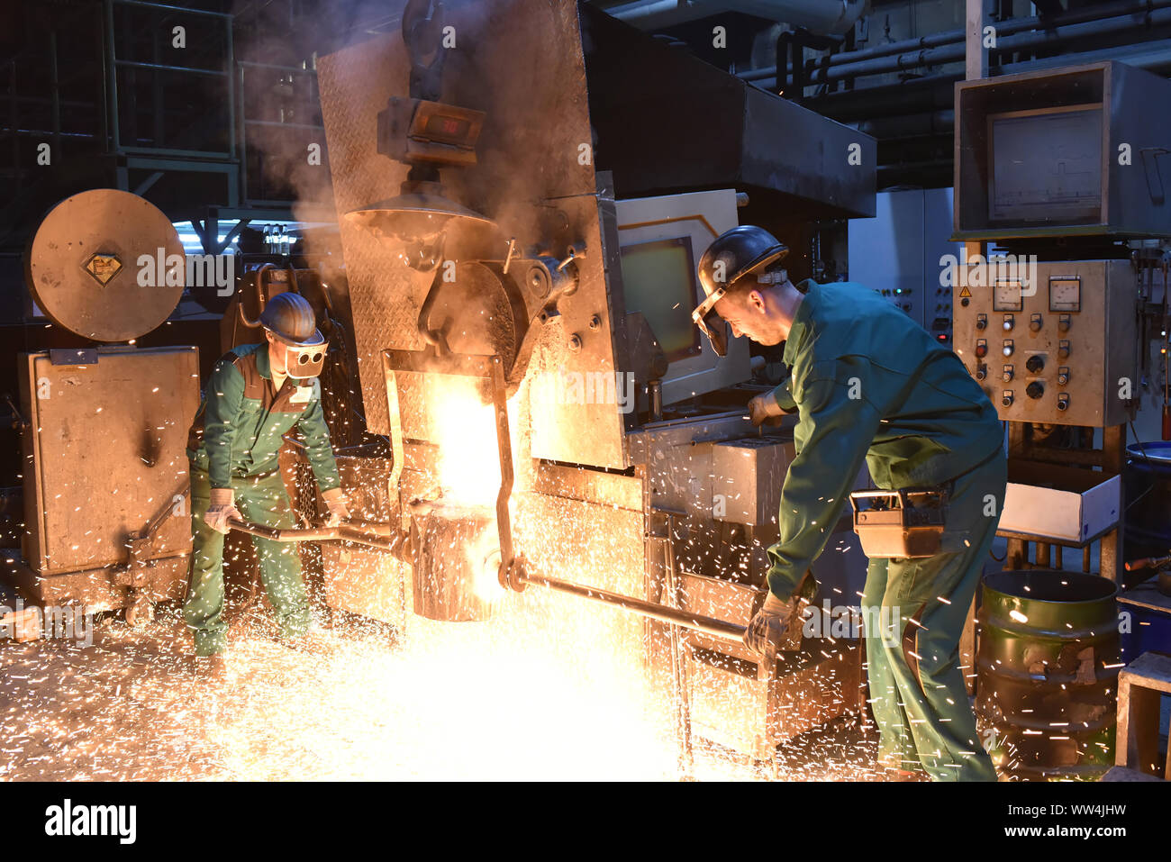 I lavoratori in un getto di fonderia di un pezzo di metallo - Sicurezza sul lavoro e il lavoro di squadra Foto Stock