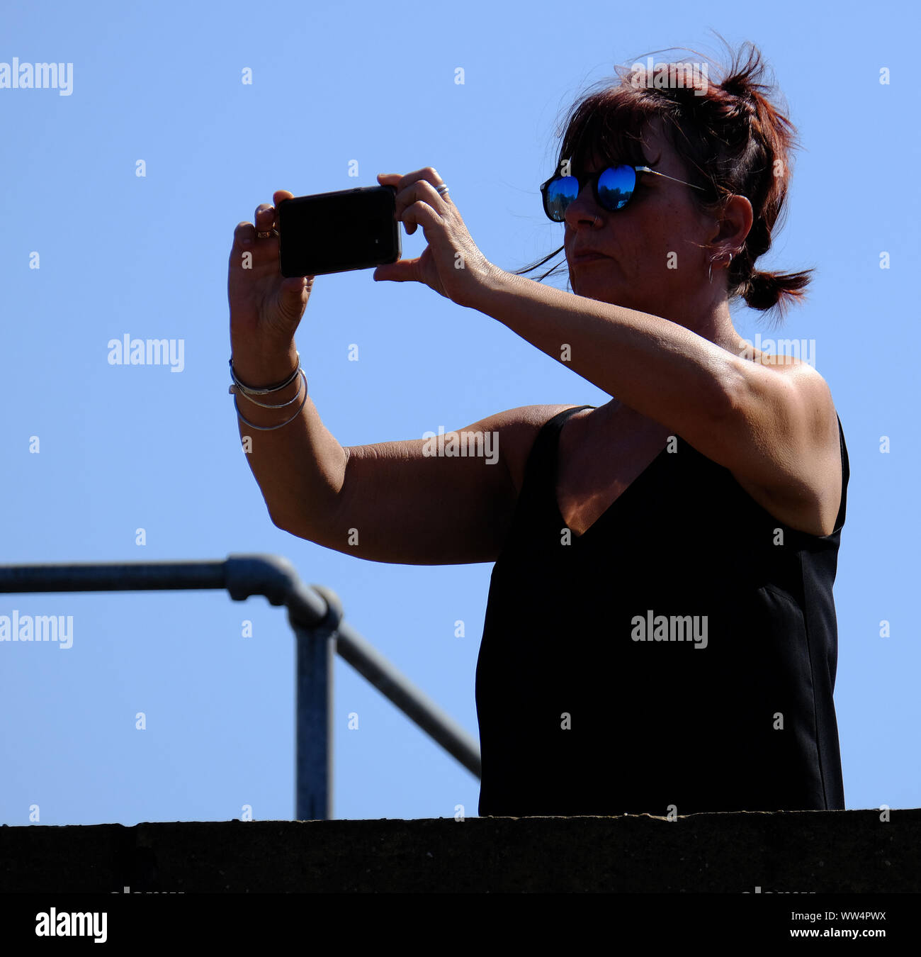 La donna nel sole luminoso tenendo fotografia con la fotocamera del cellulare. Foto Stock