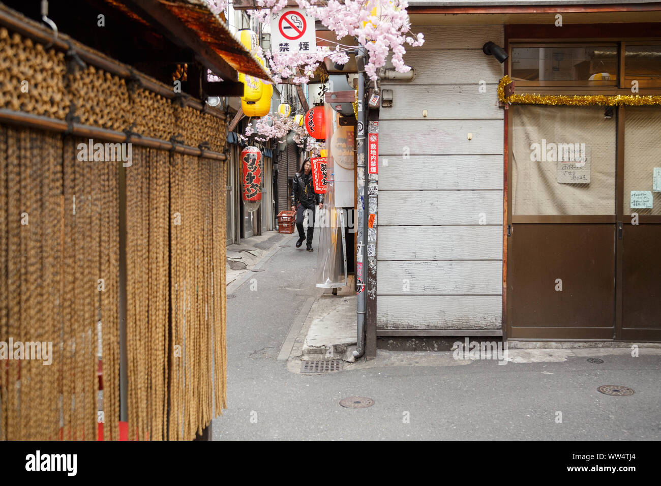 Un uomo giapponese avvicinando in stretto vicolo di via di izakayas e minuscolo diners stipati chiamato Omoide Yokocho in Shinjuku, Tokyo, Giappone. Foto Stock