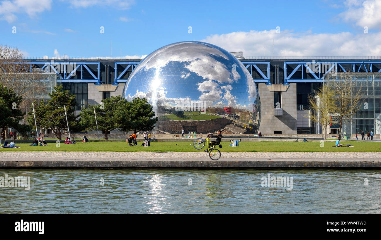 Parigi, Francia - 19 Marzo 2019: le persone che si godono la primavera soleggiata nel Parc de la Villette. Un uomo sta eseguendo un wheelie stunt con la sua moto. Foto Stock