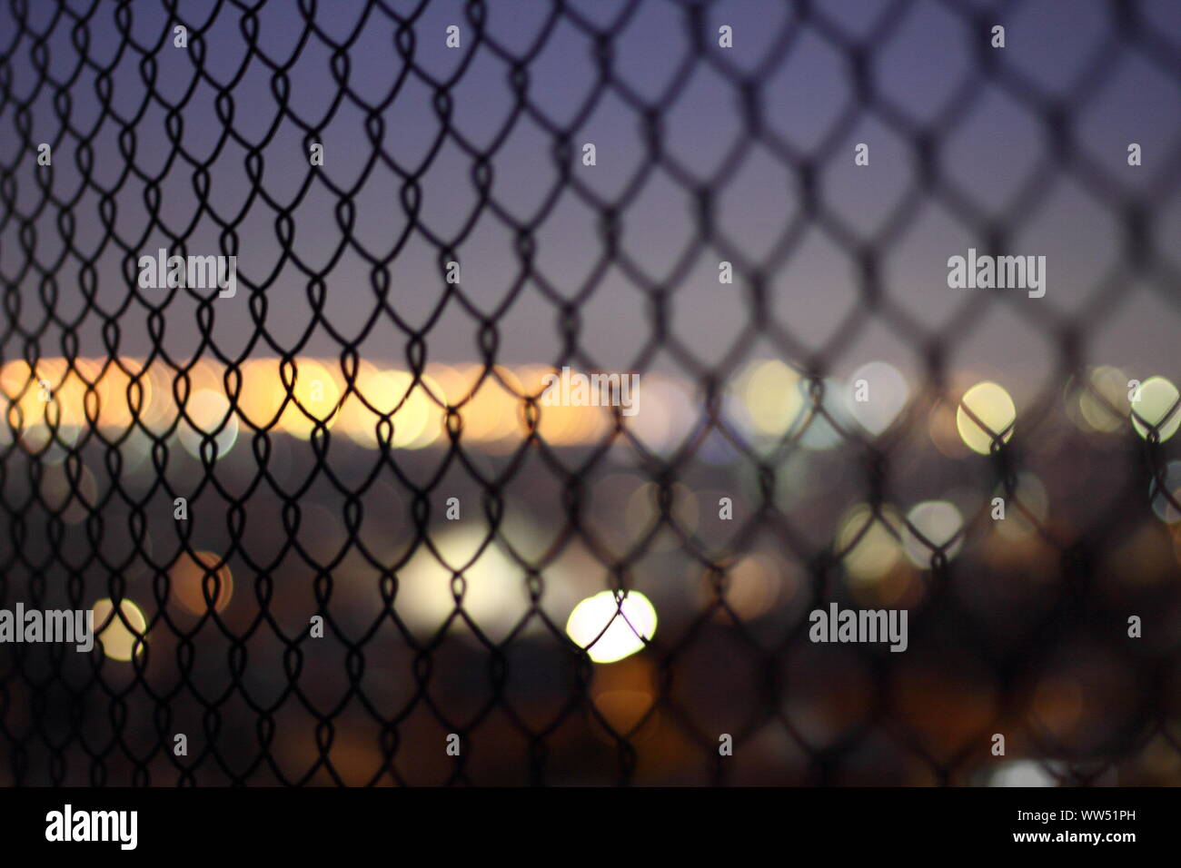 Le luci della città attraverso un filo di maglia recinzione, Foto Stock