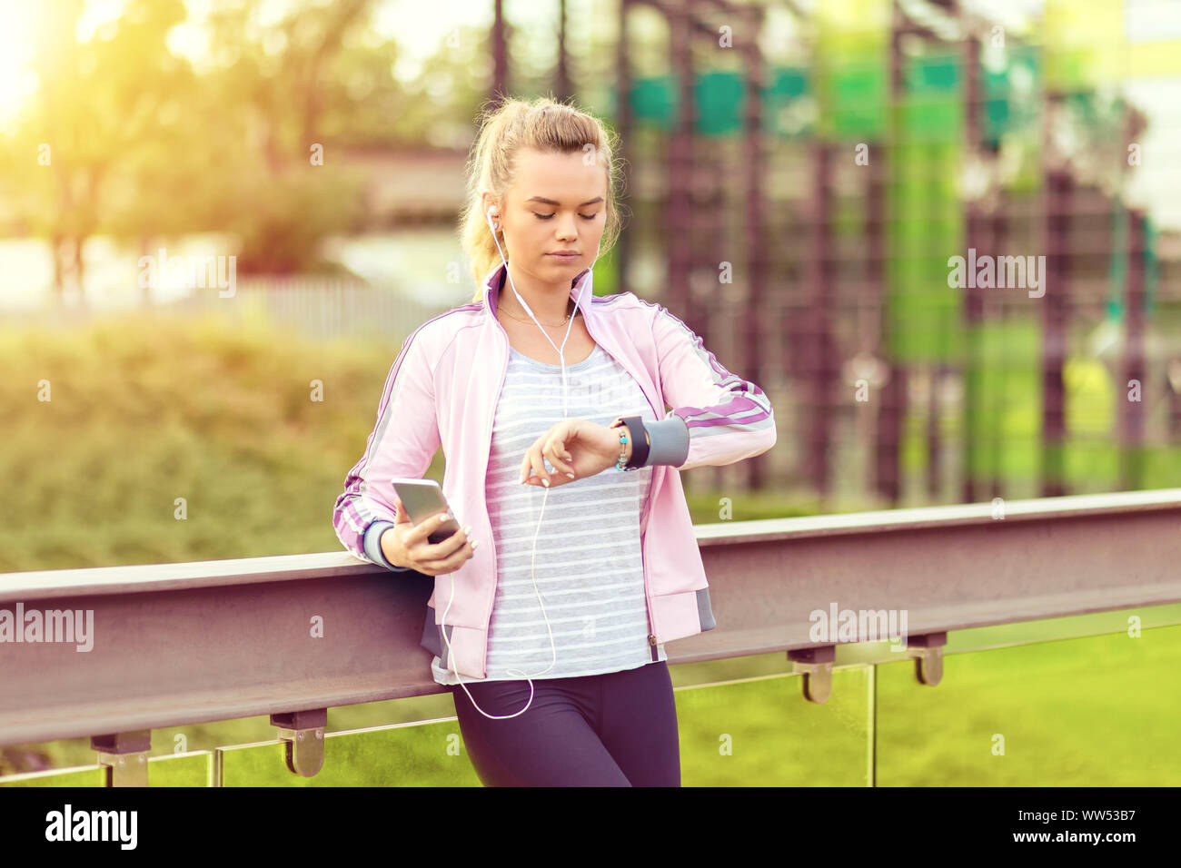 Atleta giovane ragazza ascoltando musica durante l'allenamento al parco smartwatch di regolazione prima di jogging Foto Stock