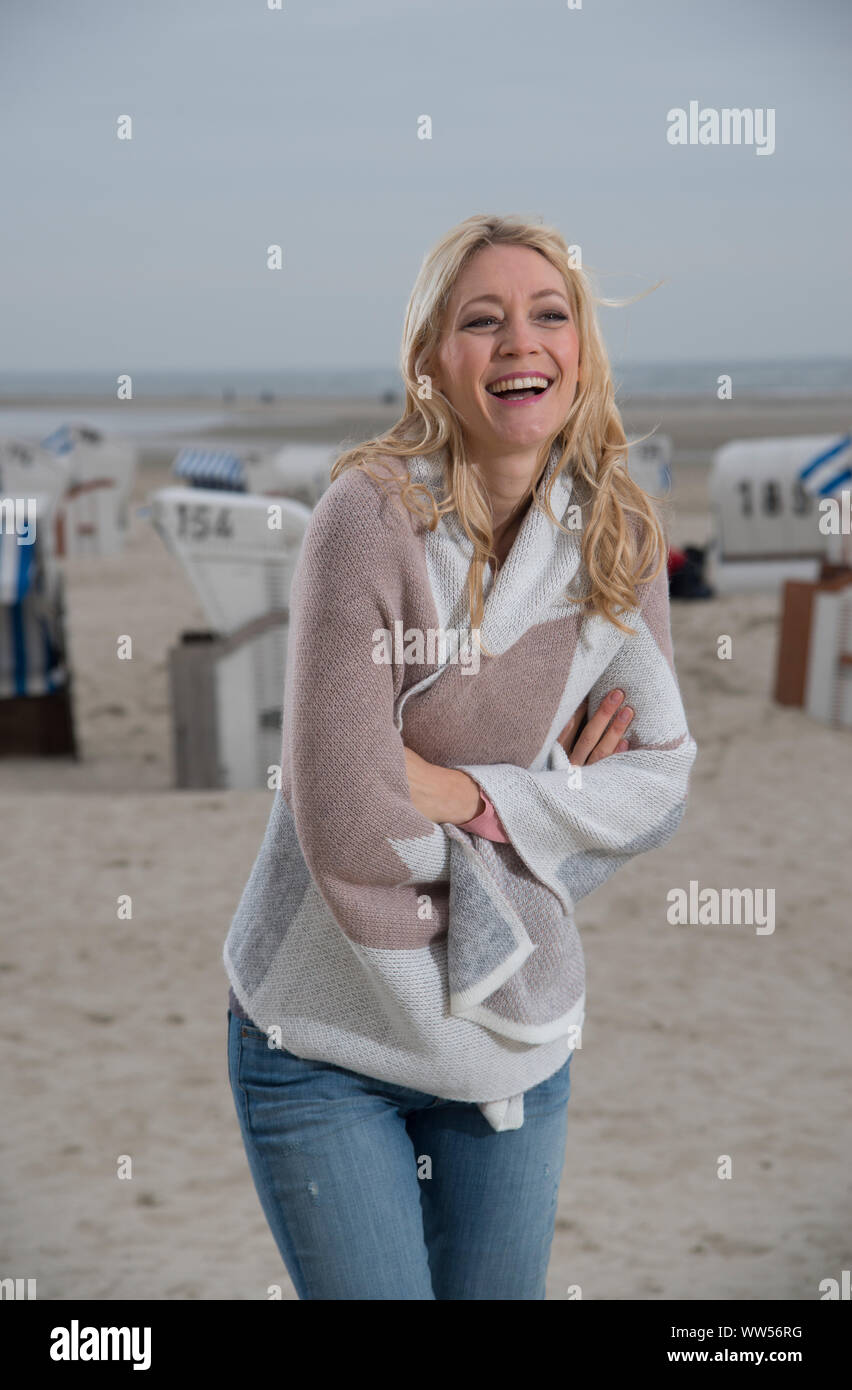Donna con bracci incrociati e cardigan ridere di fronte spiaggia, sedie Foto Stock