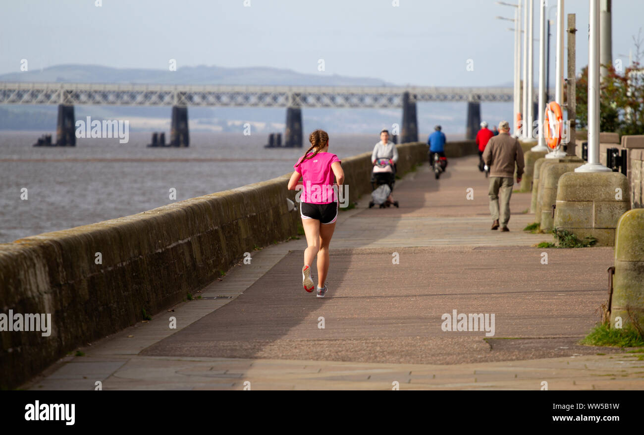 Dundee, Tayside, Scozia, Regno Unito, 13 Settembre 2019: Regno Unito Meteo. In autunno il sole di mattina con una fresca brezza fresca di Dundee. Un pareggiatore femmina jogging lungo la passeggiata del lungomare cittadino e con una vista del famoso 1800's Tay ponte ferroviario in distanza. Credito: Dundee fotografico / Alamy Live News Foto Stock