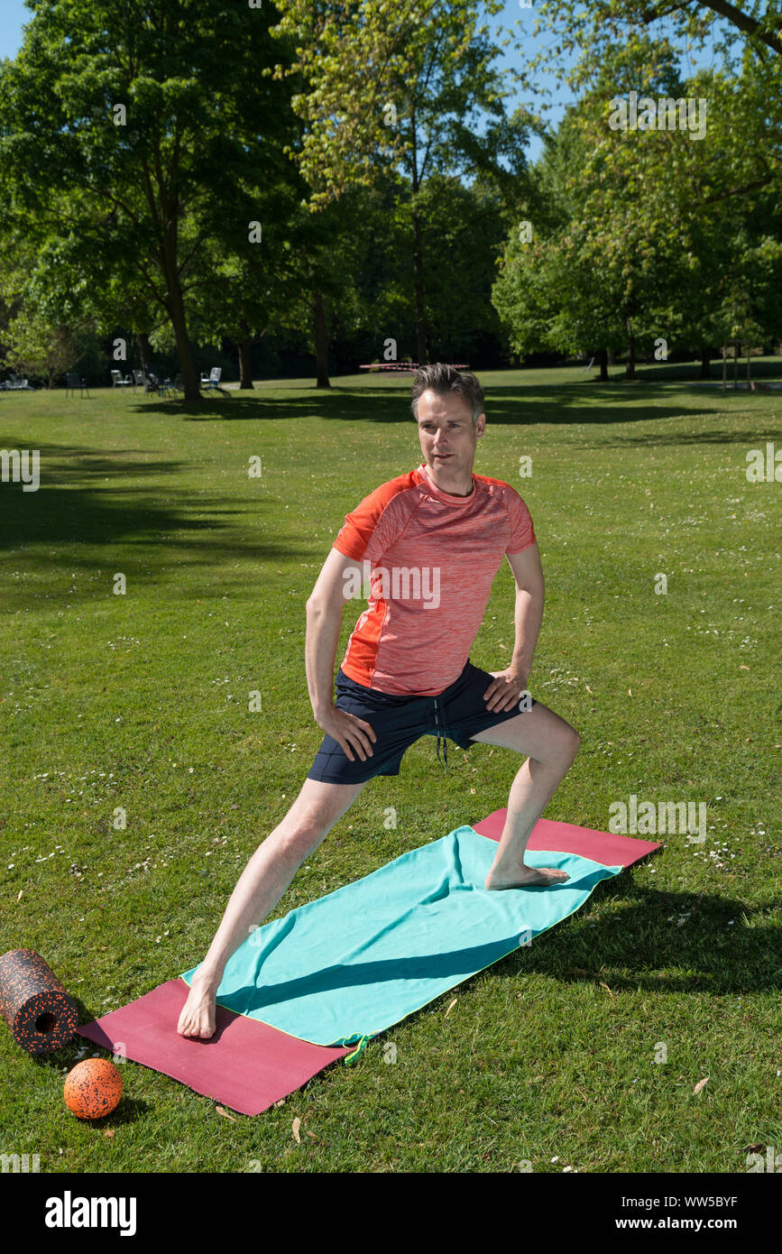 Uomo in abbigliamento sportivo nel parco sul tappetino, ginnastica, stretching esercizio, stretching gamba Foto Stock