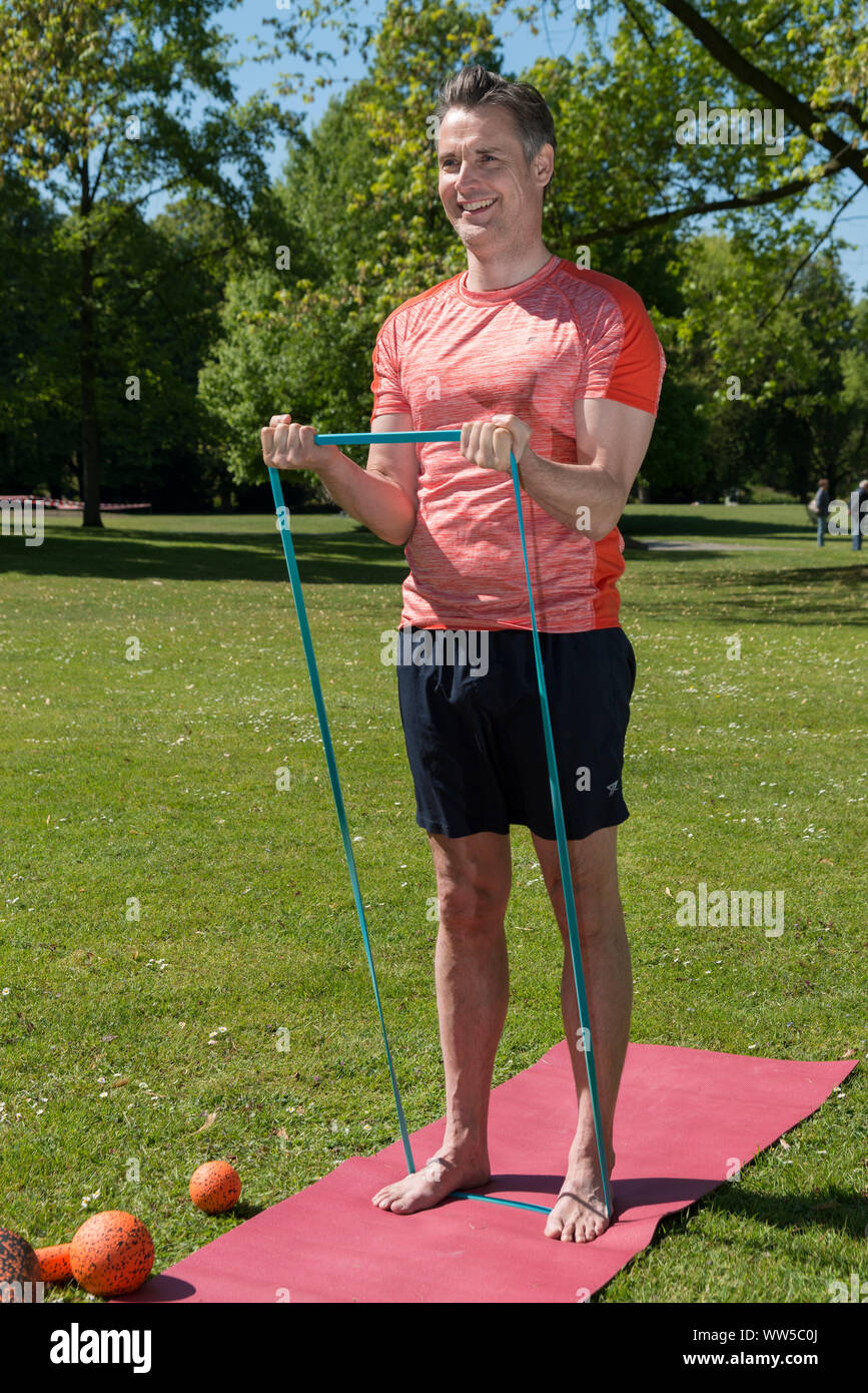 Uomo in abbigliamento sportivo sul tappeto nel parco, pratica, fitness, ginnastica ribbon Foto Stock