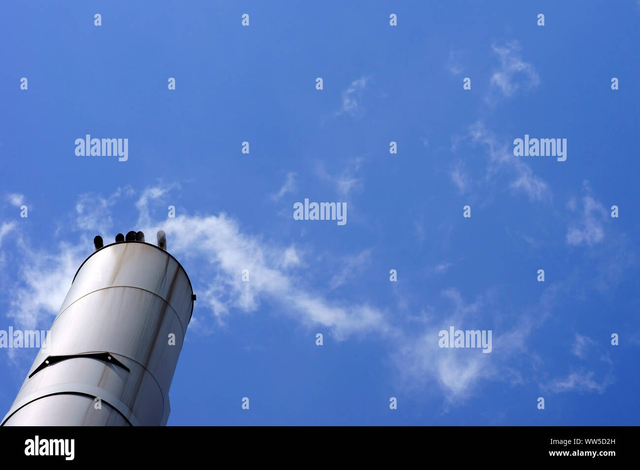 Il fumo in acciaio inox fumaioli di una piccola stazione di alimentazione nella parte anteriore di un cielo blu, Foto Stock