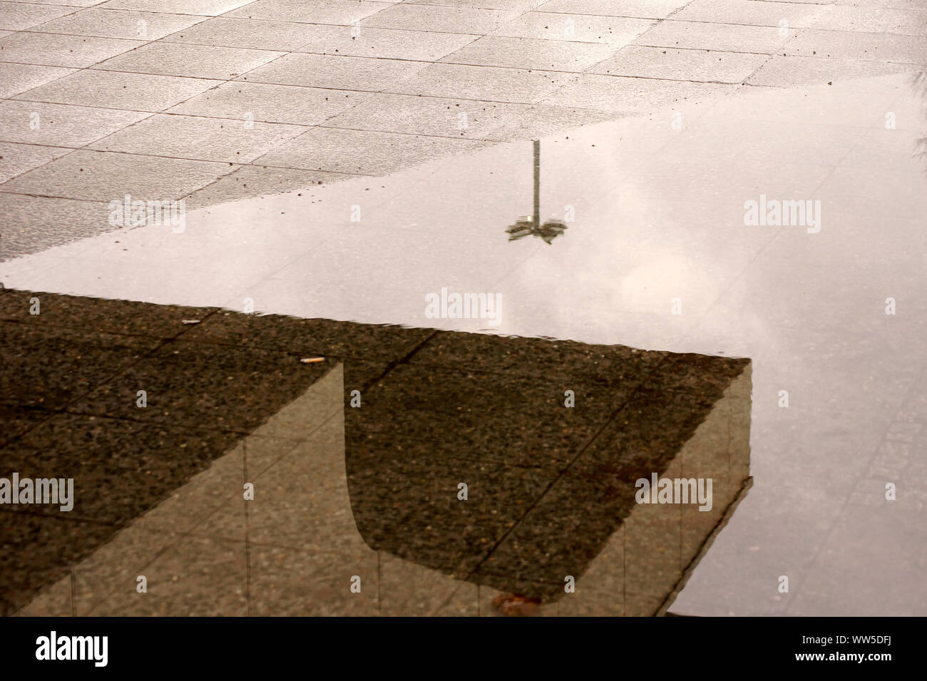 Bordo del tetto e di una lanterna si riflettono in una pozza di pioggia su un marciapiede, Foto Stock