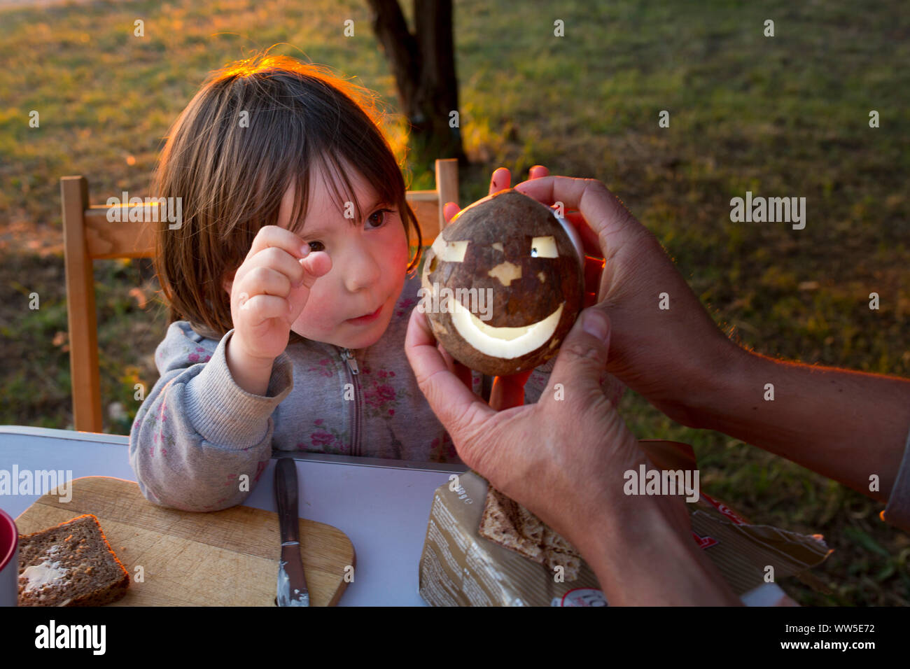 4-6 anni ragazza in un campeggio tavolo, stupito da una noce di cocco con il volto luminoso Foto Stock