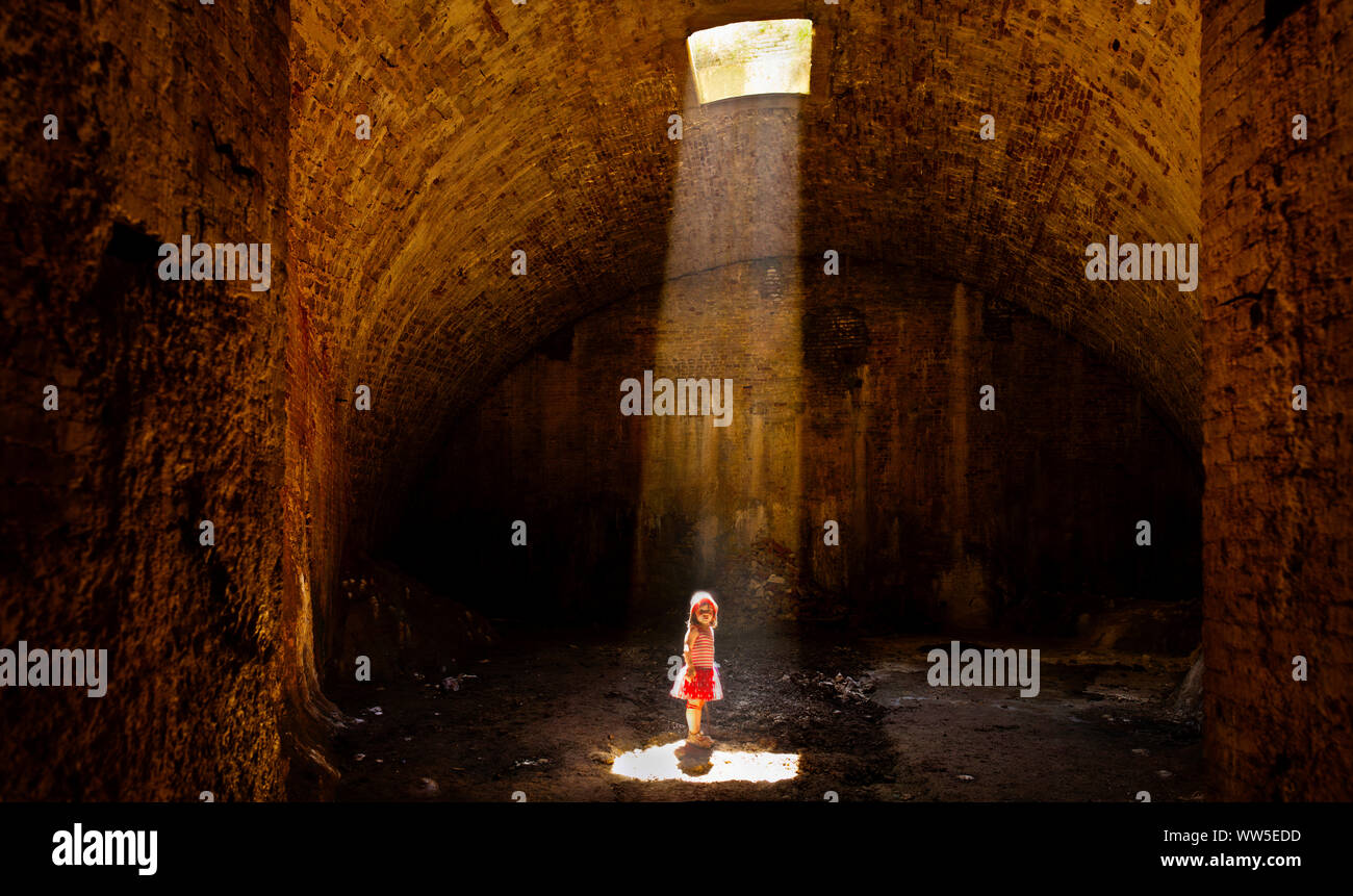 4-6 anni ragazza in abito a strisce in cantina in piedi nel cono di luce Foto Stock