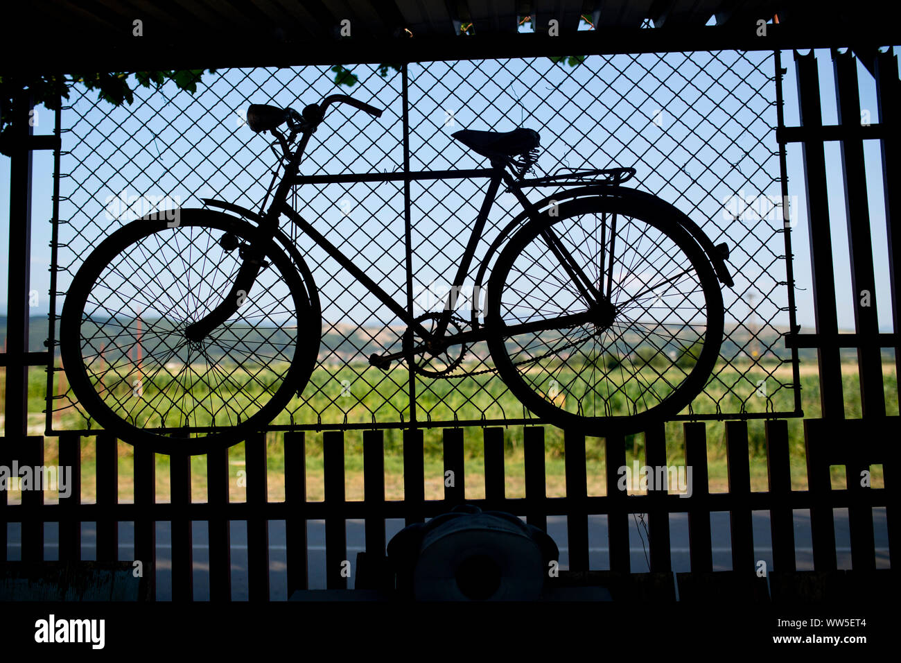 Vecchia bicicletta appesa sul muro della griglia nella parte anteriore del campo verde Foto Stock
