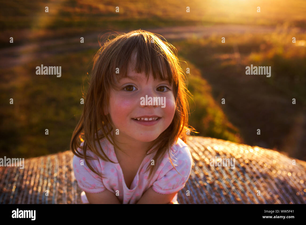 4-6 anni ragazza seduta sulla balla di fieno, sorridente nella fotocamera, luce della sera Foto Stock