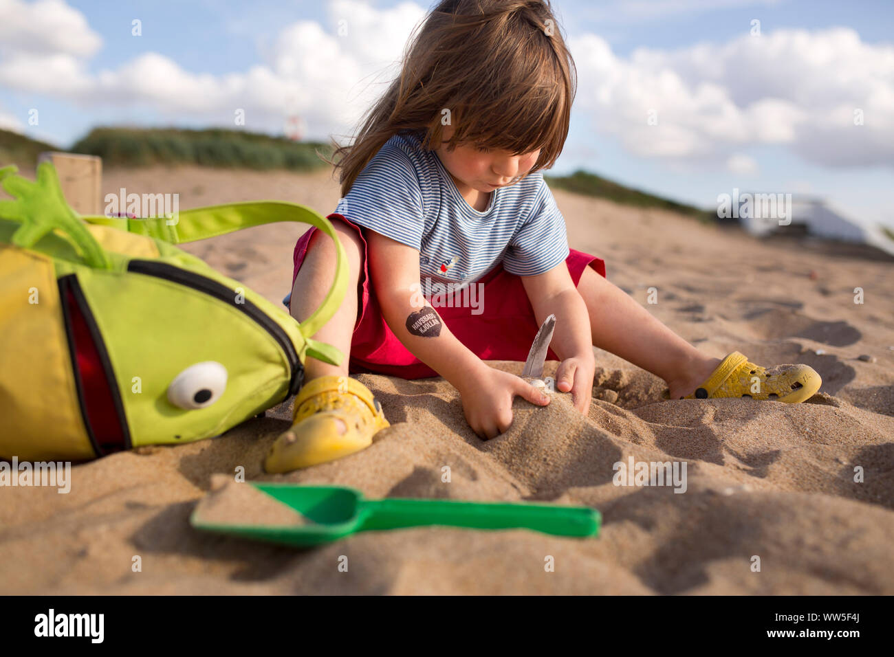 4-6 anni ragazza con pantaloni rossi e rana zaino giocando nella sabbia sulla spiaggia Foto Stock