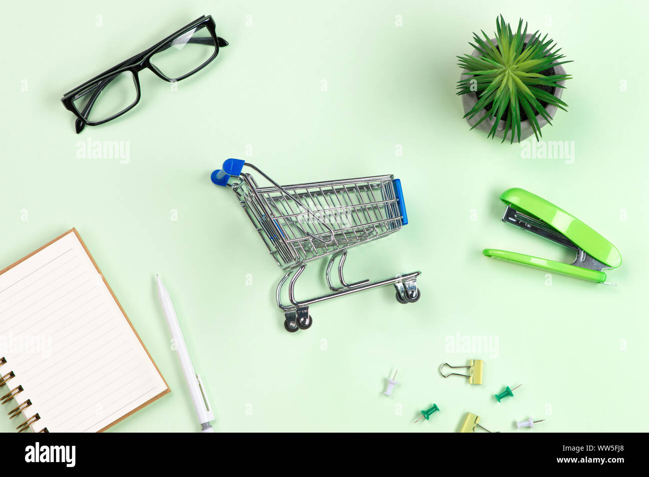 Lo shopping online concetto. piccolo blu carrello e forniture per ufficio su sfondo verde Foto Stock