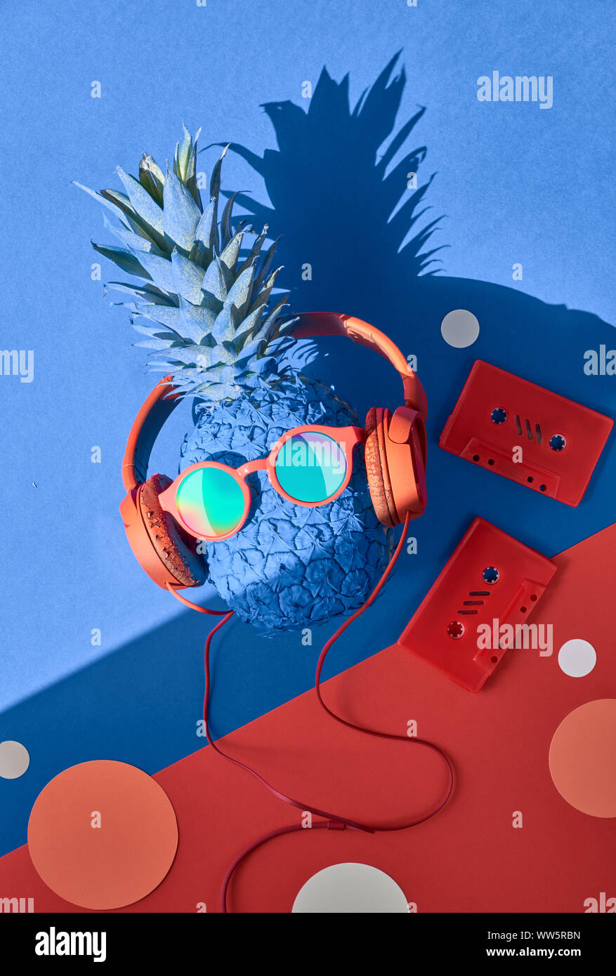 Funny ananas in occhiali da sole e auricolari con un'ombra, piatto adagiare sulla carta blu sullo sfondo Foto Stock