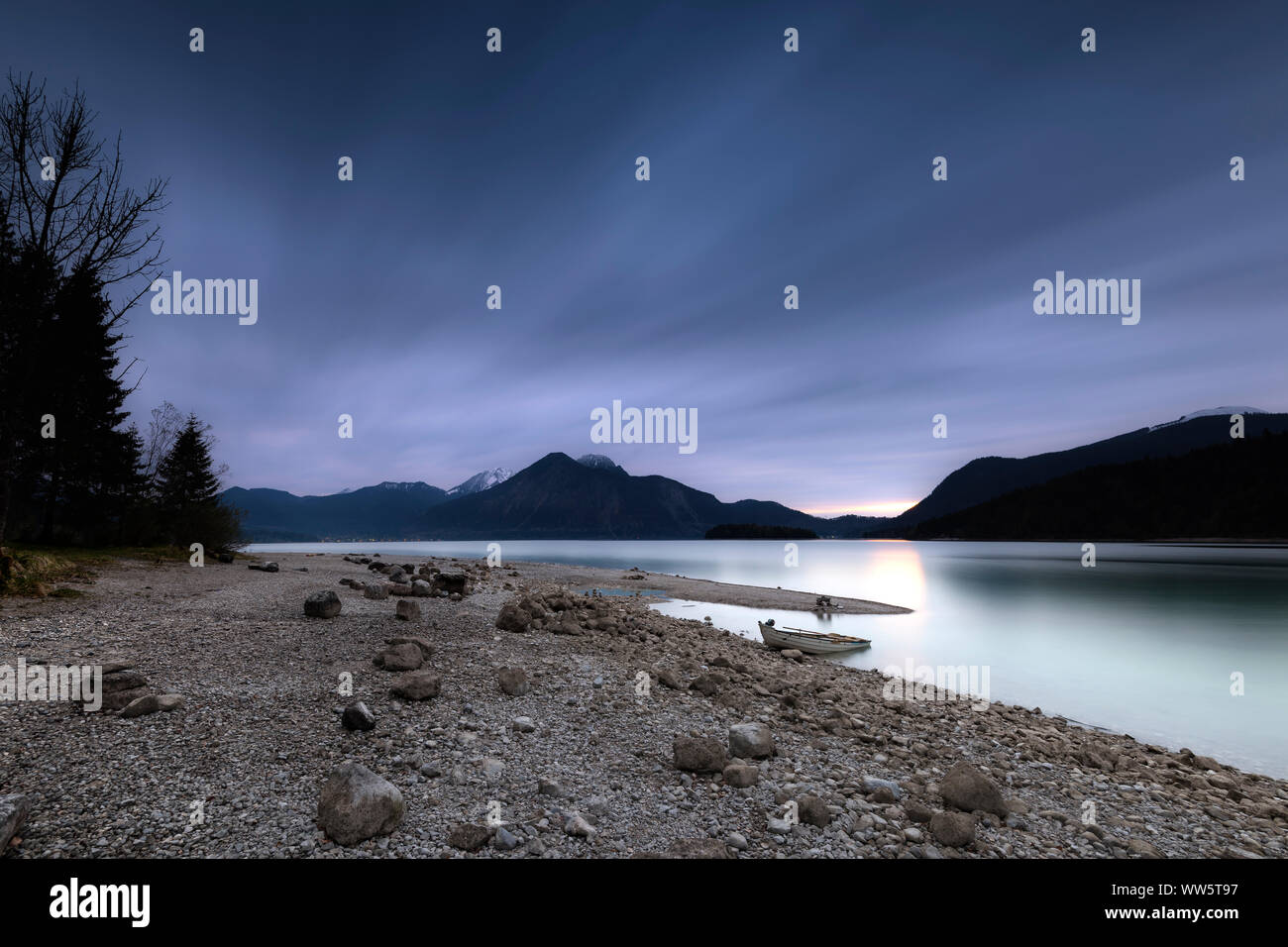 Barca a remi sulla riva del Walchensee poco dopo il tramonto e sullo sfondo la Monaco di Baviera backyard montagne Herzogstand, Heimgarten e Jochberg Foto Stock