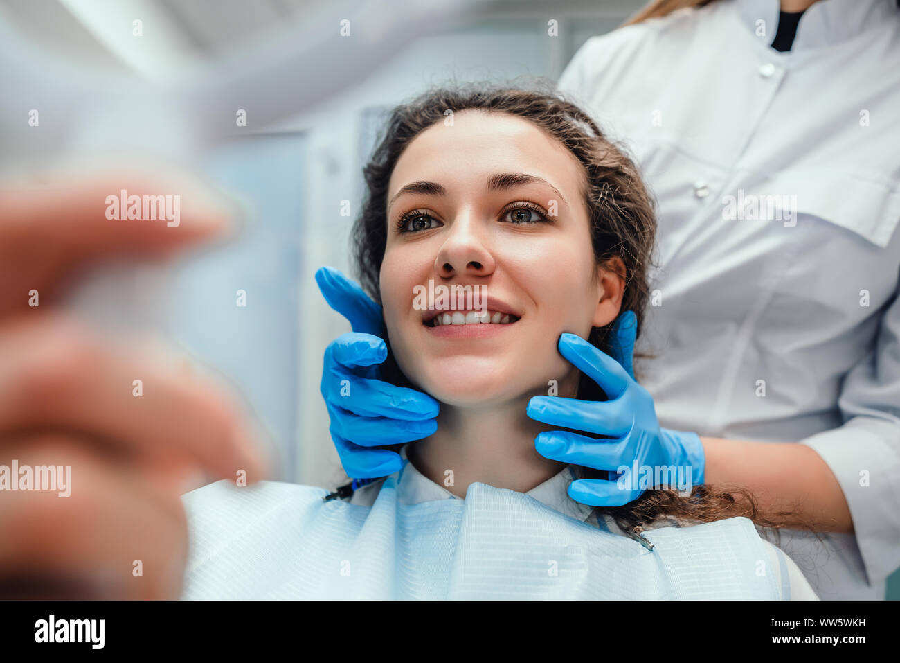 La sanità e la medicina concetto.donna felice paziente guardando nello specchio in corrispondenza dei denti, seduto in poltrona odontoiatrica. messa a fuoco selettiva. Foto Stock