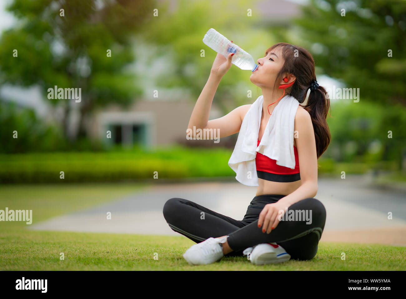 Asian attraente sportivo da donna in abito rosso acqua potabile da una bottiglia dopo il jogging o in esecuzione mentre era seduto in posizione di parcheggio. Foto Stock